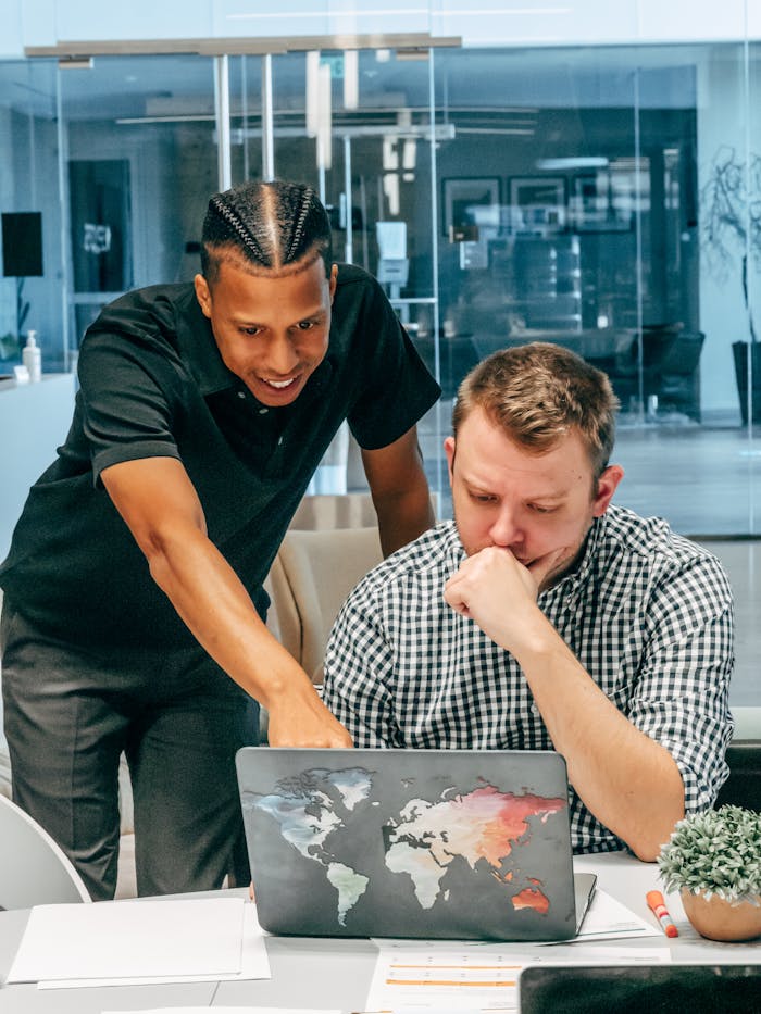 Two men working together in a modern office, focusing on a laptop screen.